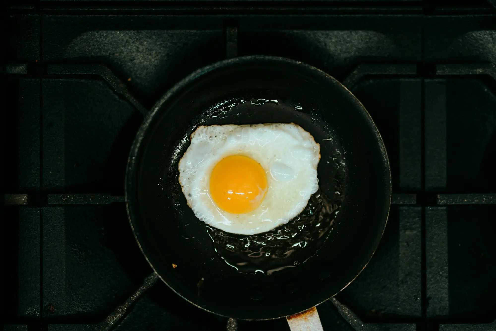 A fried egg in a black frying pan on a gas hob