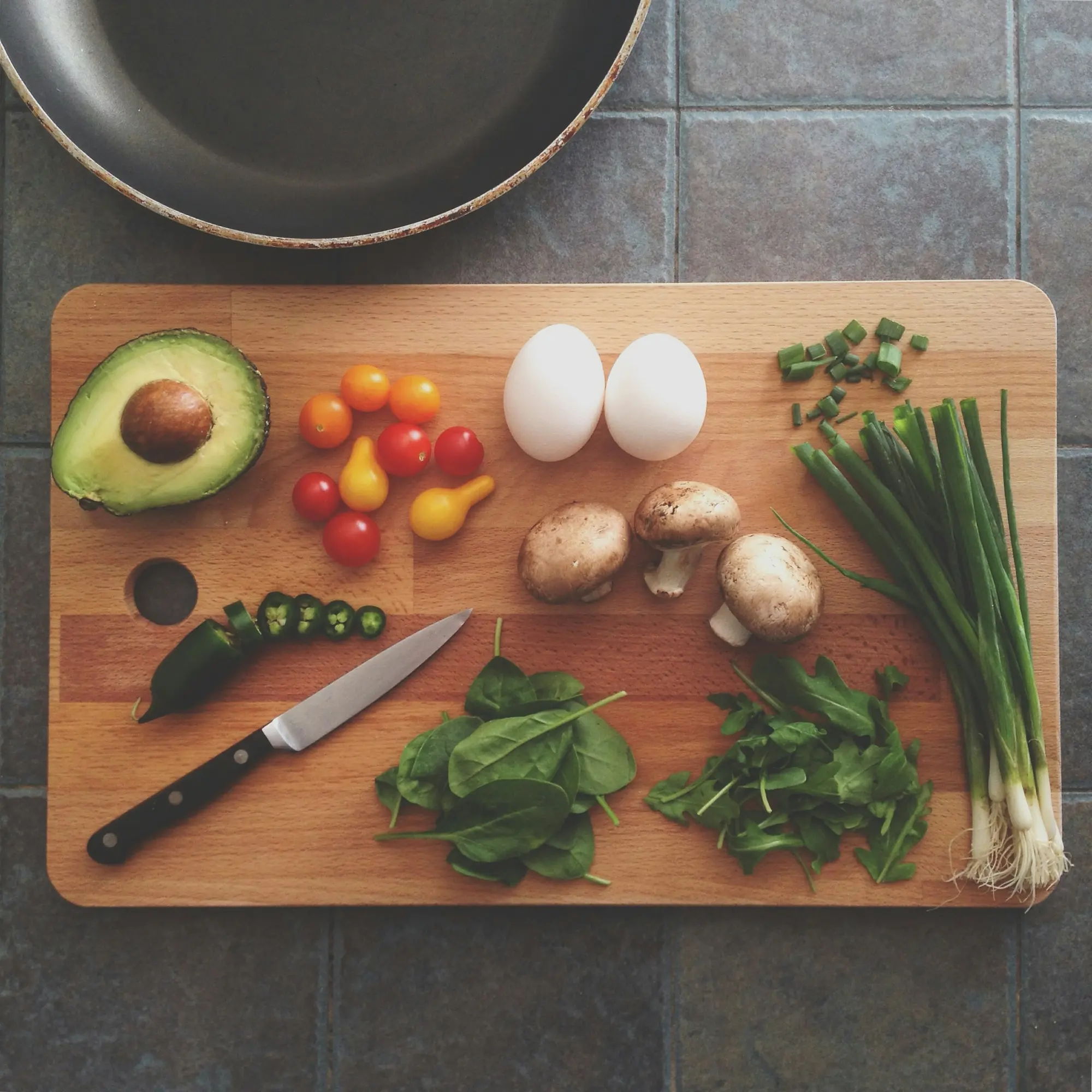 Avocado, eggs, tomatoes, mushrooms and spring onions on a chopping board