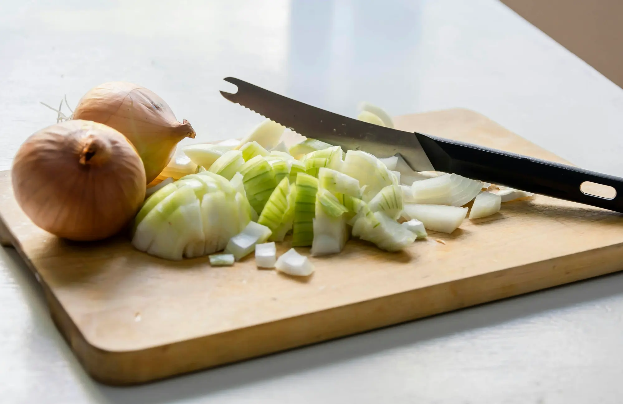 A chopped onion and a knife on a wooden chopping board