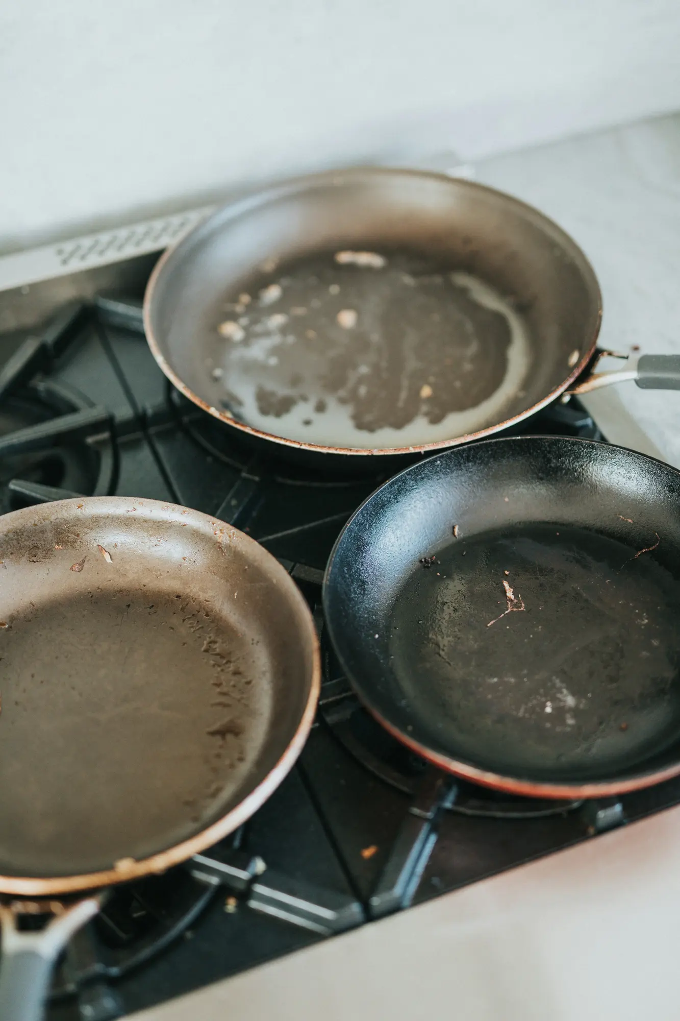 A stainless steel frying pan beside a black frying pan on a gas hob