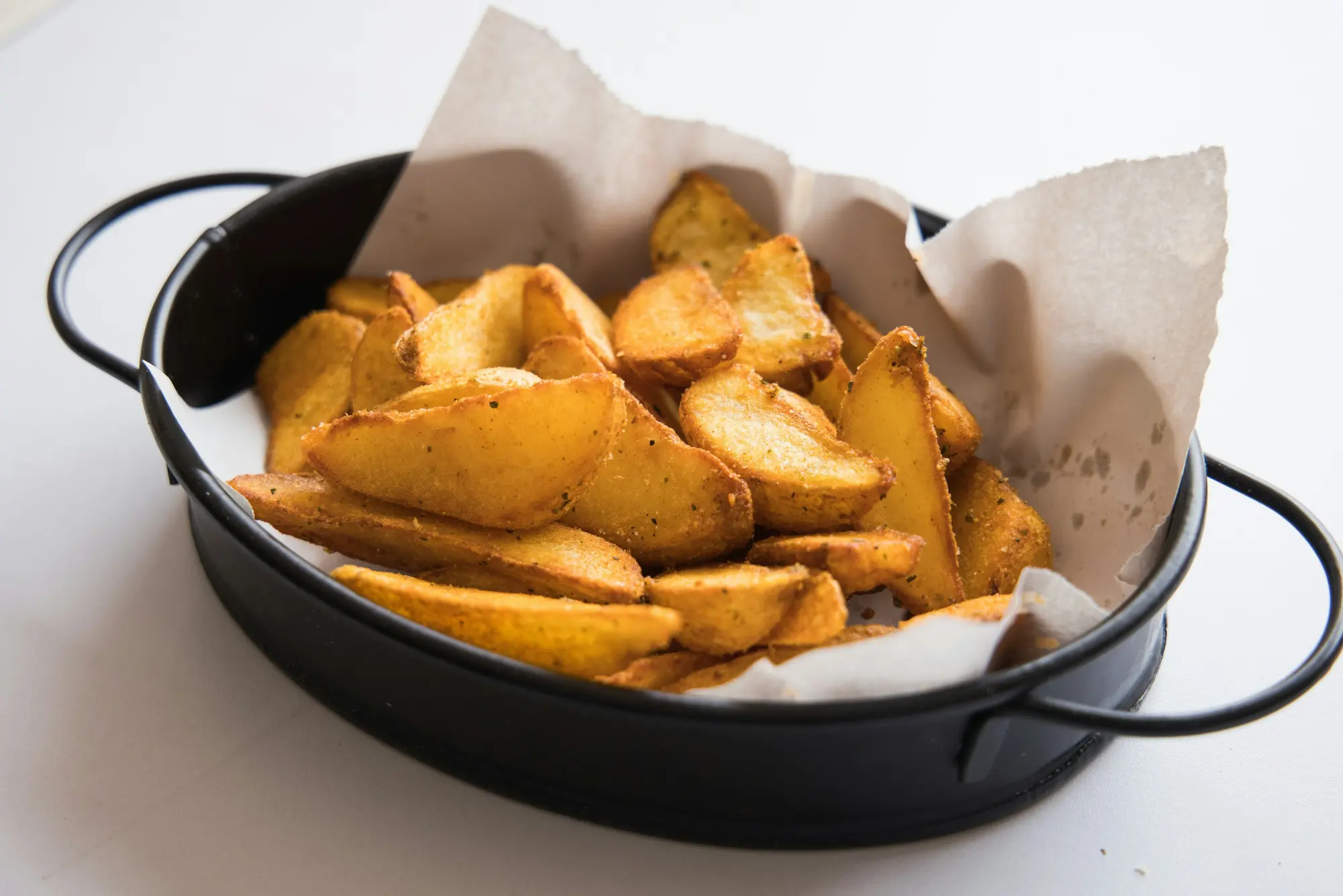 Golden potato wedges in a dark dish lined with baking paper